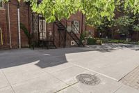 an old brick building with a staircase and sidewalk on both sides of a street with plants growing on the sidewalk