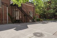 an old brick building with a staircase and sidewalk on both sides of a street with plants growing on the sidewalk