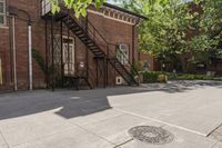 an old brick building with a staircase and sidewalk on both sides of a street with plants growing on the sidewalk