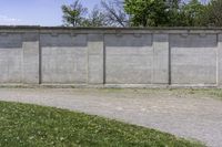 a cement wall next to a sidewalk with grass and trees in the background of the wall is filled with weeds