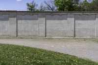 a cement wall next to a sidewalk with grass and trees in the background of the wall is filled with weeds