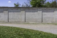 a cement wall next to a sidewalk with grass and trees in the background of the wall is filled with weeds