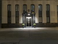 a large stone building with a black door at night with some plants inside the doors