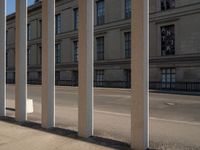 an outdoor area with pillars that are leaning against the side of a building, with cars passing by on the sidewalk below