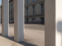 an outdoor area with pillars that are leaning against the side of a building, with cars passing by on the sidewalk below