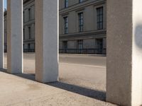 an outdoor area with pillars that are leaning against the side of a building, with cars passing by on the sidewalk below