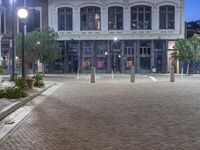 a very nice looking building on a brick sidewalk at night with some street lights and plants