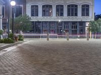 a very nice looking building on a brick sidewalk at night with some street lights and plants