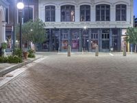 a very nice looking building on a brick sidewalk at night with some street lights and plants