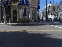 people are walking down the road near a store with blue and white awnings