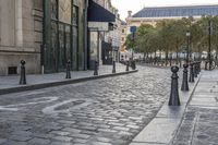 a cobble stone street with green gate post holders in front of buildings and cars