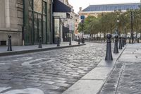 a cobble stone street with green gate post holders in front of buildings and cars