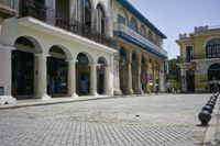 a stone paved street that has columns and blue awnings around the building on either side