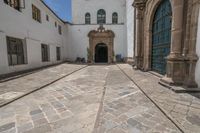 a couple of large doors near a building on some stone flooring with bicycles parked outside