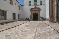 a couple of large doors near a building on some stone flooring with bicycles parked outside