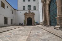 a couple of large doors near a building on some stone flooring with bicycles parked outside