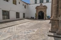 a couple of large doors near a building on some stone flooring with bicycles parked outside