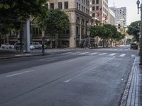 an empty street in the middle of the city with some cars driving down it and buildings