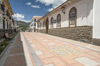 a long brick street with a line of buildings with arches in them and a sidewalk with tiles in front