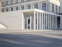 the large, empty sidewalk with multiple columns in front of the building with two signs