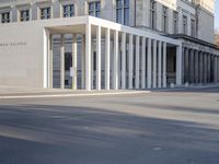 the large, empty sidewalk with multiple columns in front of the building with two signs