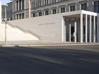 the large, empty sidewalk with multiple columns in front of the building with two signs