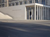 the large, empty sidewalk with multiple columns in front of the building with two signs