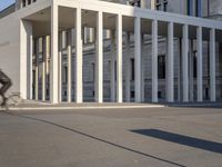 the large, empty sidewalk with multiple columns in front of the building with two signs