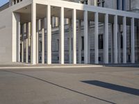 the large, empty sidewalk with multiple columns in front of the building with two signs