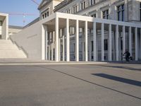 the large, empty sidewalk with multiple columns in front of the building with two signs