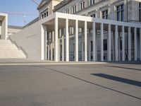 the large, empty sidewalk with multiple columns in front of the building with two signs