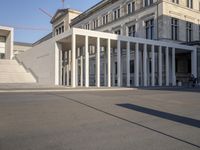 the large, empty sidewalk with multiple columns in front of the building with two signs