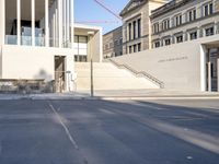 the large, empty sidewalk with multiple columns in front of the building with two signs