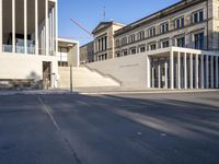 the large, empty sidewalk with multiple columns in front of the building with two signs