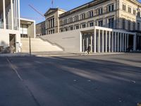 the large, empty sidewalk with multiple columns in front of the building with two signs