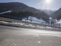 an empty road and snow covered hills in the background as a car passes through the photo