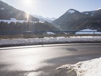 an empty road and snow covered hills in the background as a car passes through the photo
