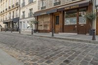 an empty street in front of a cafe with lots of windows and wooden doors on it