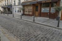 an empty street in front of a cafe with lots of windows and wooden doors on it