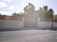 a gate and wall with palm trees in the background at an intersection near a street