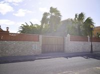 a gate and wall with palm trees in the background at an intersection near a street