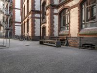 a bench sits in the middle of a courtyard with parked bicycles nearby and tall brick buildings