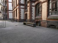 a bench sits in the middle of a courtyard with parked bicycles nearby and tall brick buildings