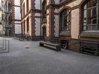 a bench sits in the middle of a courtyard with parked bicycles nearby and tall brick buildings