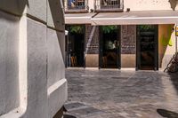 people walk in the empty streets near small tables and umbrellas and a building with balconies on the windows