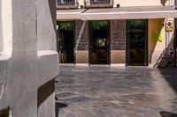 people walk in the empty streets near small tables and umbrellas and a building with balconies on the windows