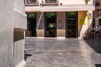 people walk in the empty streets near small tables and umbrellas and a building with balconies on the windows