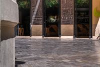 people walk in the empty streets near small tables and umbrellas and a building with balconies on the windows