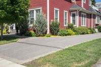 a large brick house with white windows next to a sidewalk and green trees on either side of the street