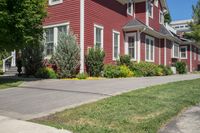 a large brick house with white windows next to a sidewalk and green trees on either side of the street